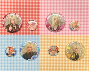 May include: A collection of six round pinback buttons featuring portraits of a person with blonde hair. The buttons vary in size and have glitter and heart accents. The background is a mix of pink, blue, and orange gingham.