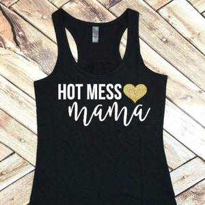 Puede incluir: Camiseta de tirantes negra con el texto "HOT MESS mama" en blanco con un corazón de purpurina dorada.