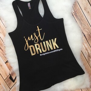 May include: Black tank top with gold lettering that says "just drunk" and the hashtag "#bridgettebecomesBRIDEgette".