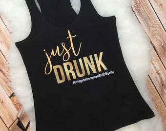 Puede incluir: Camiseta de tirantes negra con letras doradas que dicen "just drunk" y el hashtag "#bridgettebecomesBRIDEgette".