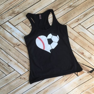 Pode incluir: Camisola de alças preta com um design em forma de coração feito de uma bola de beisebol e uma bola de futebol. O coração é branco com costuras vermelhas na bola de beisebol e costuras pretas na bola de futebol.