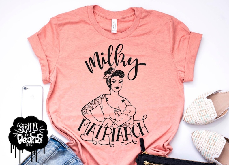 May include: A peach-colored t-shirt with a black graphic of a woman breastfeeding a baby with the text "Milky Matriarch".