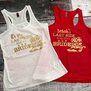 Puede incluir: Dos camisetas sin mangas blancas con texto dorado y un par de botas de vaquero doradas. El texto en la camiseta blanca dice "It's My Last Ride Before I'm A Bride". El texto en la camiseta roja dice "Sarah's Last Ride Before She's A Bride".