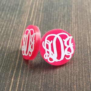 May include: A pair of pink glitter earrings with white monogram initials.