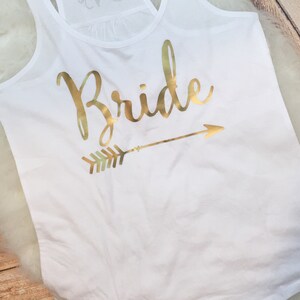 May include: White tank top with a gold glitter design that says "Bride" with an arrow pointing to the right.