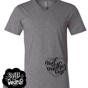 May include: A heather grey V-neck t-shirt with the text "and another one" in a black heart shape on the right side of the shirt.