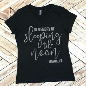 May include: Black v-neck t-shirt with the text "In memory of sleeping -til- noon #MAMALIFE" in silver glitter.