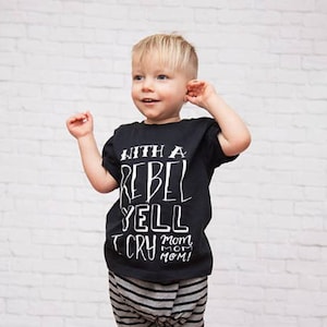 May include: A young child wearing a black t-shirt with white text that reads "With a Rebel Yell I Cry Mom Mom Mom!"