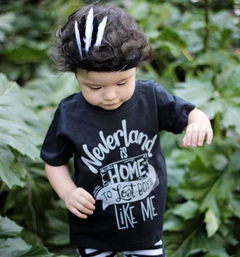 May include: A black t-shirt with a white graphic that says "Neverland is Home to Lost Boys Like Me". A young child is wearing the shirt and has a black and white feather headband in their hair.