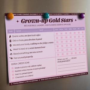 Puede incluir: Una lista de verificación Grown-up Gold Stars de color lavanda, sujeta por tres imanes de colores. La lista de verificación incluye tareas como beber agua, hacer tareas y leer. También es visible el texto "BECAUSE BILLS, LAUNDRY, AND FLOSSING DESERVE APPLAUSE".
