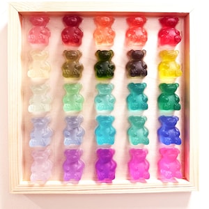 May include: A wooden framed display of colorful gummy bear candies. The bears are arranged in rows and columns, showcasing a spectrum of colors including red, orange, green, blue, and purple. The candies are translucent, and the frame is made of light-colored wood.