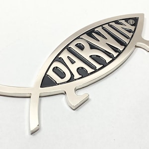May include: A silver-colored fish symbol with the word "DARWIN" in black lettering inside. The symbol has a small loop on the top and a bottle opener on the bottom.