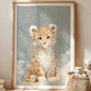 Op de afbeelding: Een ingelijste kunstdruk met een aquarelillustratie van een baby luipaard. De welp heeft bruine en beige vlekken en zit op een wolk tegen een zachte blauwe achtergrond met sterren. Een rieten mand met teddyberen staat in de buurt.