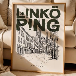 May include: A framed art print featuring a black and white illustration of a street scene in Linköping, Sweden. The word "LINKÖPING" is printed in dark green at the top. The print is displayed on a beige background.