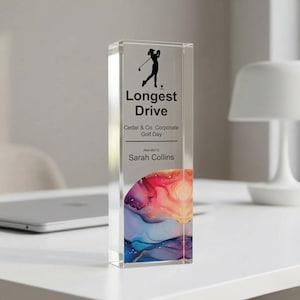 May include: A clear acrylic trophy with the words "Longest Drive" and a silhouette of a golfer. The trophy is for the Cedar & Co. Corporate Golf Day and awarded to Sarah Collins. The bottom features a colorful abstract design.