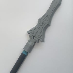 May include: A gray spear with a detailed blade design. The spear features a dark gray shaft and a gray head with intricate carvings. The spear's head is approximately 12 inches long.