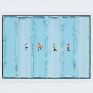 May include: A framed abstract painting with a white border. The artwork features a textured, light blue background with vertical lines. Tiny figures of people with beach gear are depicted, including a surfer with a yellow board and a person with a pink inflatable.