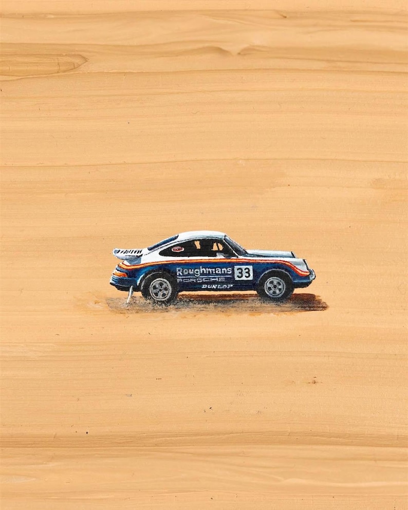 K&ouml;nnte beinhalten: Ein Miniatur-Porsche-Rennwagen in Blau, Wei&szlig; und Orange mit der Nummer 33 auf der Seite. Auf dem Auto stehen die Worte "Roughmans Porsche Dunlop" aufgedruckt. Das Auto steht vor einem beigen Hintergrund.