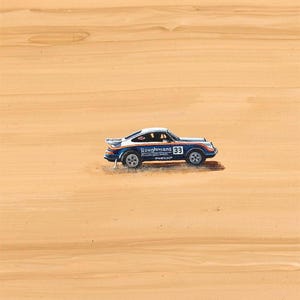 K&ouml;nnte beinhalten: Ein kleines blau-wei&szlig;es Rennauto mit dem Text "Roughmans 33" an der Seite. Das Auto hat einen Spoiler und ist vor einem hellbraunen Hintergrund platziert.