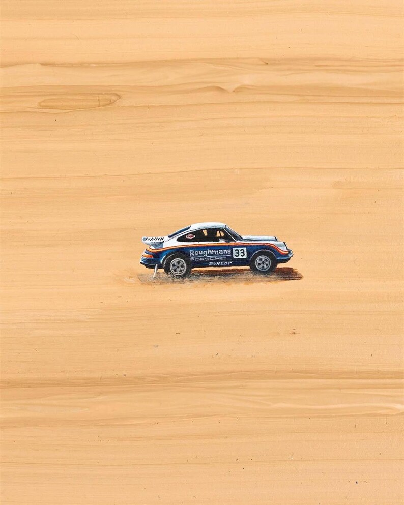 K&ouml;nnte beinhalten: Ein kleines blau-wei&szlig;es Rennauto mit dem Text "Roughmans 33" an der Seite. Das Auto hat einen Spoiler und ist vor einem hellbraunen Hintergrund platziert.