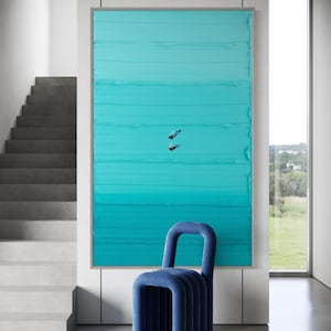May include: A teal blue abstract painting with horizontal brushstrokes, depicting two figures diving underwater. The painting is framed and hanging on a white wall, with a blue chair in the foreground.