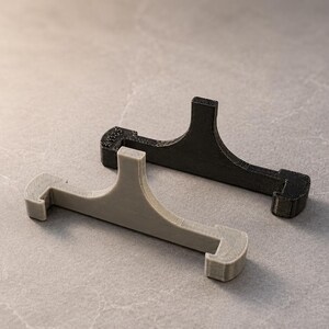 May include: Two T-shaped display stands, one in matte black and one in light gray, featuring a horizontal base with hooked ends and a central vertical support arm. The black stand has the text 3DMS embossed on the left side of the base.