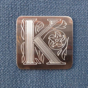 May include: A silver metal bookmark with an engraved letter K and floral design.