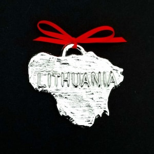 May include: Silver ornament shaped like the outline of Lithuania with the word "Lithuania" embossed on the surface. The ornament is attached to a red ribbon.