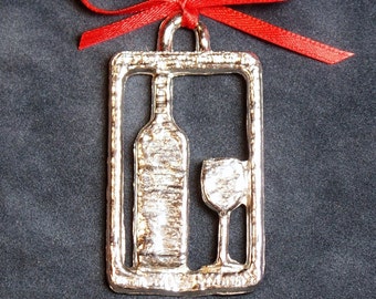 Puede incluir: Adorno navideño plateado en forma de botella de vino y vaso. El adorno está decorado con una cinta roja.