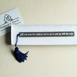 May include: A silver bookmark with a blue tassel. The bookmark has the quote "If you want the rainbow, you've got to put up with the rain." engraved on it.