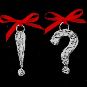 May include: Two silver ornaments with red ribbon bows. One ornament is a question mark and the other is a long, thin, pointed shape.