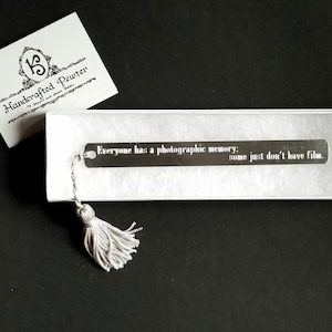 May include: Silver bookmark with a tassel. The bookmark has the text "Everyone has a photographic memory: some just don't have film."