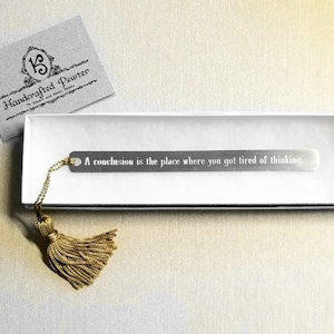 May include: A silver bookmark with a gold tassel and the quote "A conclusion is the place where you got tired of thinking." The bookmark is in a white box with a gray card that says "Handcrafted Pewter by Stuart and Karen Smith".