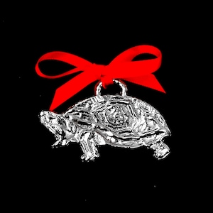 May include: A silver turtle ornament with a red bow. The turtle is detailed with a textured shell and has a loop for hanging.