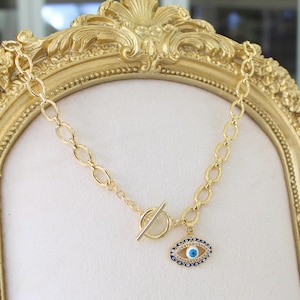 May include: A gold chain necklace with a blue and white evil eye charm. The chain has a toggle clasp.