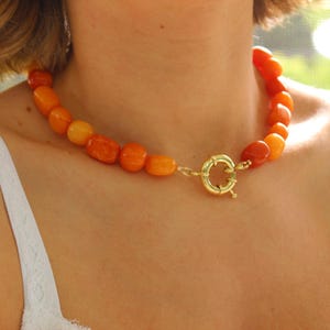 Puede incluir: Un collar de cuentas gruesas de color naranja y amarillo graduado con un cierre de palanca dorado.