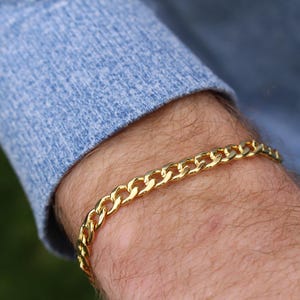 Puede incluir: Un brazalete de cadena dorada con un diseño de eslabones de curb.