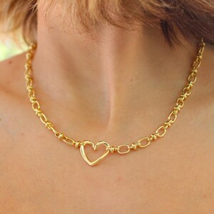 May include: Gold-toned necklace featuring a heart-shaped pendant. The necklace has a chain-link design with a heart-shaped clasp. The jewelry is worn around the neck.