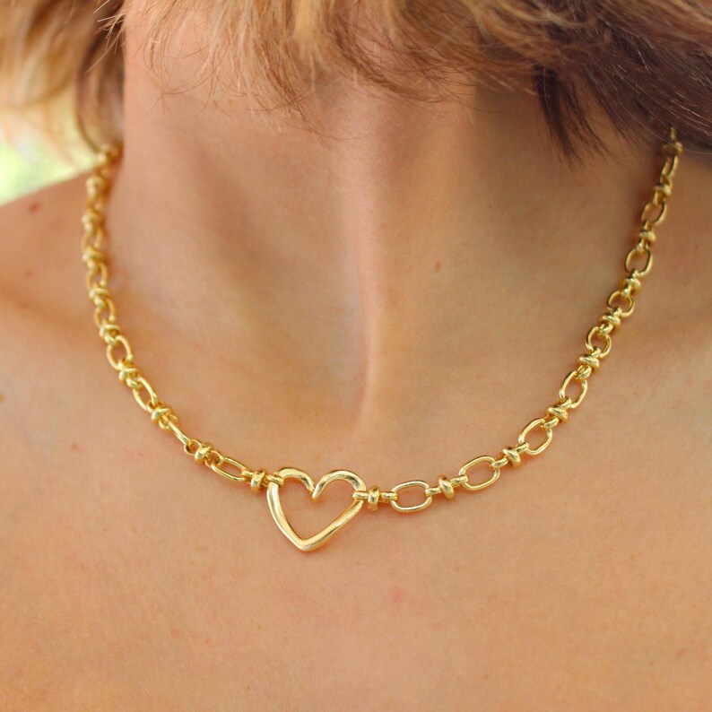May include: Gold-toned necklace featuring a heart-shaped pendant. The necklace has a chain-link design with a heart-shaped clasp. The jewelry is worn around the neck.
