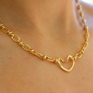 May include: Gold-toned necklace featuring a heart pendant. The necklace has a chain-link design with a heart-shaped pendant at the center. The jewelry is made of a shiny, gold-colored metal.