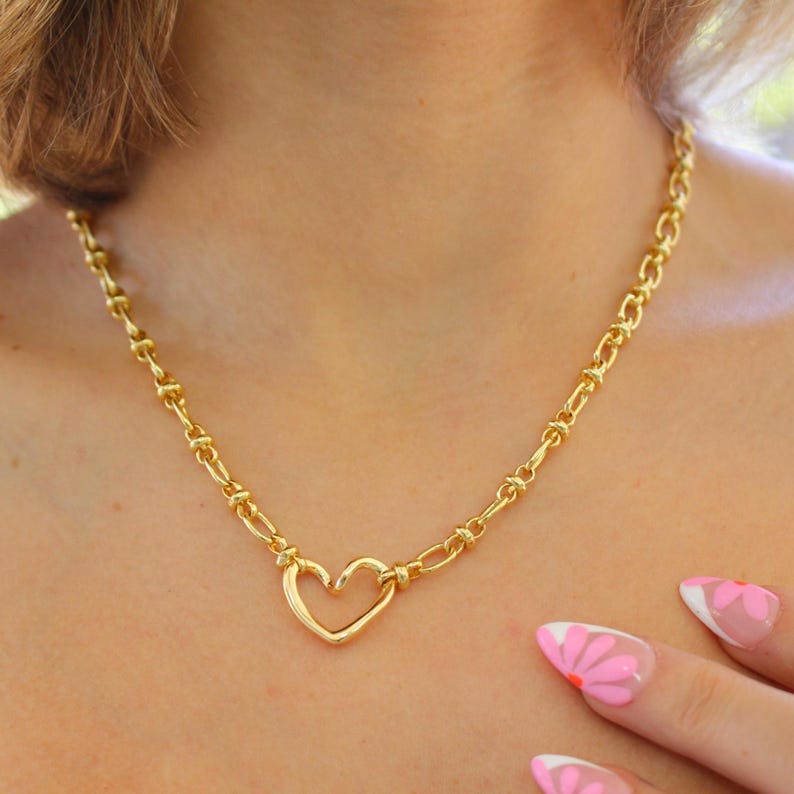 May include: Gold-toned necklace featuring a heart-shaped pendant. The necklace has a chain-link design and is worn around the neck. The heart pendant is the focal point, adding a touch of romance to the jewelry piece. The necklace is a stylish accessory.