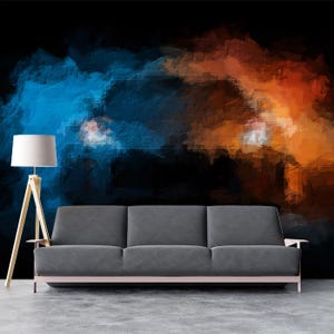 May include: A modern living room setup featuring a gray sofa with a light pink frame, a wooden tripod floor lamp with a white lampshade, and a colorful abstract wall mural in shades of blue, orange, and black. The floor is concrete.