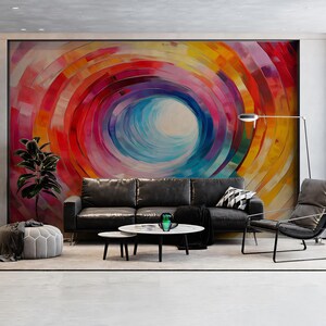 Peut inclure: Un salon moderne avec une grande peinture murale abstraite colorée aux motifs tourbillonnants de rouge, orange, jaune et bleu. Un canapé en cuir noir, une table basse ronde et un pouf gris complètent l'espace.