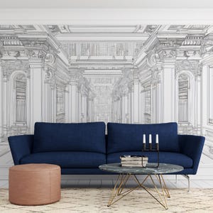 May include: A modern living room with a navy blue sofa, a round marble coffee table with gold legs, and a pink ottoman. The wall features a black and white architectural drawing of a classical building.