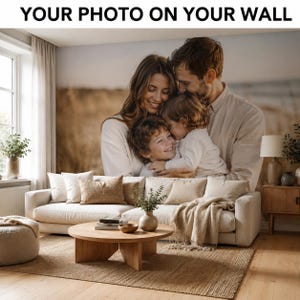 Könnte beinhalten: Ein individuelles Wandbild mit einem großformatigen Foto einer sich umarmenden Familie, das an einer Wohnzimmerwand hinter einem beigen Sofa angebracht ist. Der Text "YOUR PHOTO ON YOUR WALL" ist oben im Bild in Schwarz aufgedruckt.