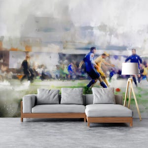 Pode incluir: Um sofá de canto cinza-claro com base de madeira está posicionado em frente a um grande mural de parede que retrata uma pintura em aquarela de jogadores de futebol com uniformes azuis e amarelos em um campo. Uma luminária de chão está à direita.