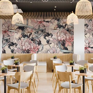 May include: A restaurant interior featuring light wood chairs with grey cushions, small round tables, and a wall mural displaying large pink and white floral illustrations with dark green foliage on a cream background, illuminated by woven pendant lights.