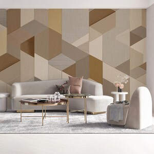 May include: A modern living room with a geometric patterned wall in shades of beige, brown, and tan. A light gray sofa, two round coffee tables, and a white armchair are in front of the wall. A patterned rug and white floor complete the scene.