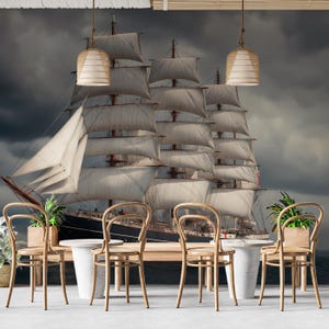 May include: A dramatic mural depicting a tall ship with white sails under a dark, stormy sky. The room features wooden chairs, a table, and pendant lights, evoking a nautical atmosphere.