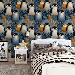 Op de afbeelding: Kinderslaapkamer met marineblauwe pinguïnbehang. De kamer heeft een wit bed met een zwart-wit patroon dekbedovertrek, een wit nachtkastje met een stervormige lamp en een ingelijste print met tekst.